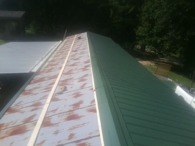 Old rusted panels beside newly installed green metal roofing — Wind Damage Roof Repair by Roofing Brothers in Lunenburg