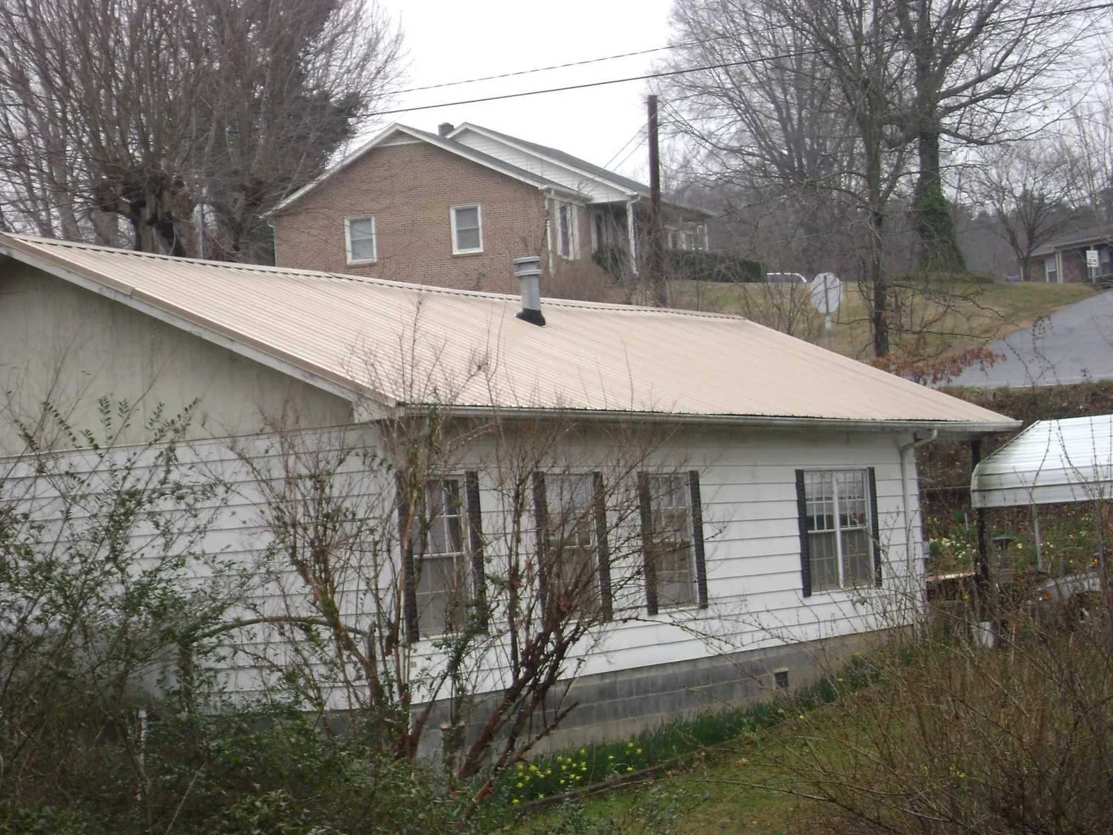 Tan metal roof on a white sided house set into a hillside — Commercial Roofing by Roofing Brothers in Lunenburg